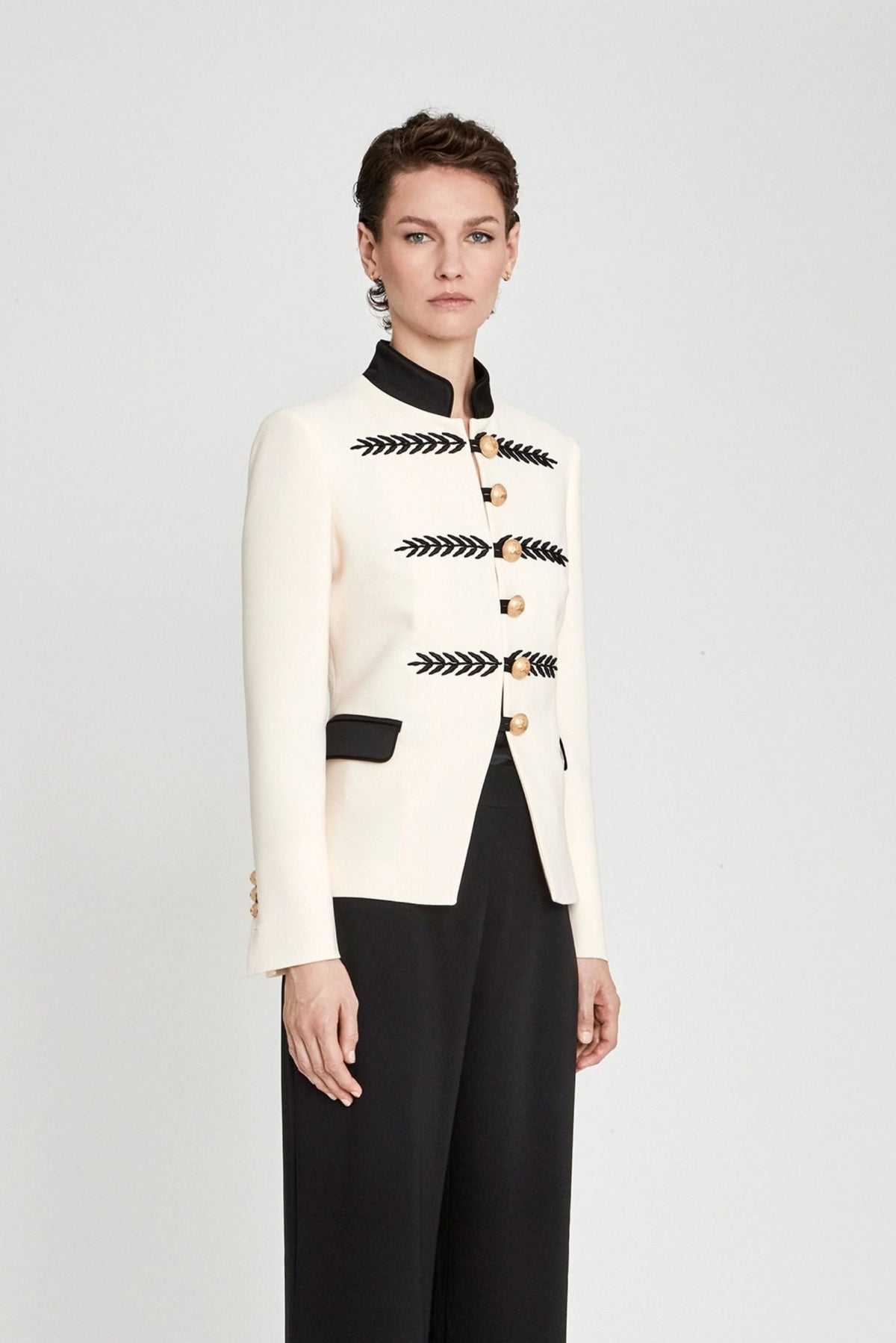 Blazer militar marfil Renata 01 corta y entallada en tejido color crema con cuello mao negro, bordados geométricos y botones dorados. Sastrería de lujo.
