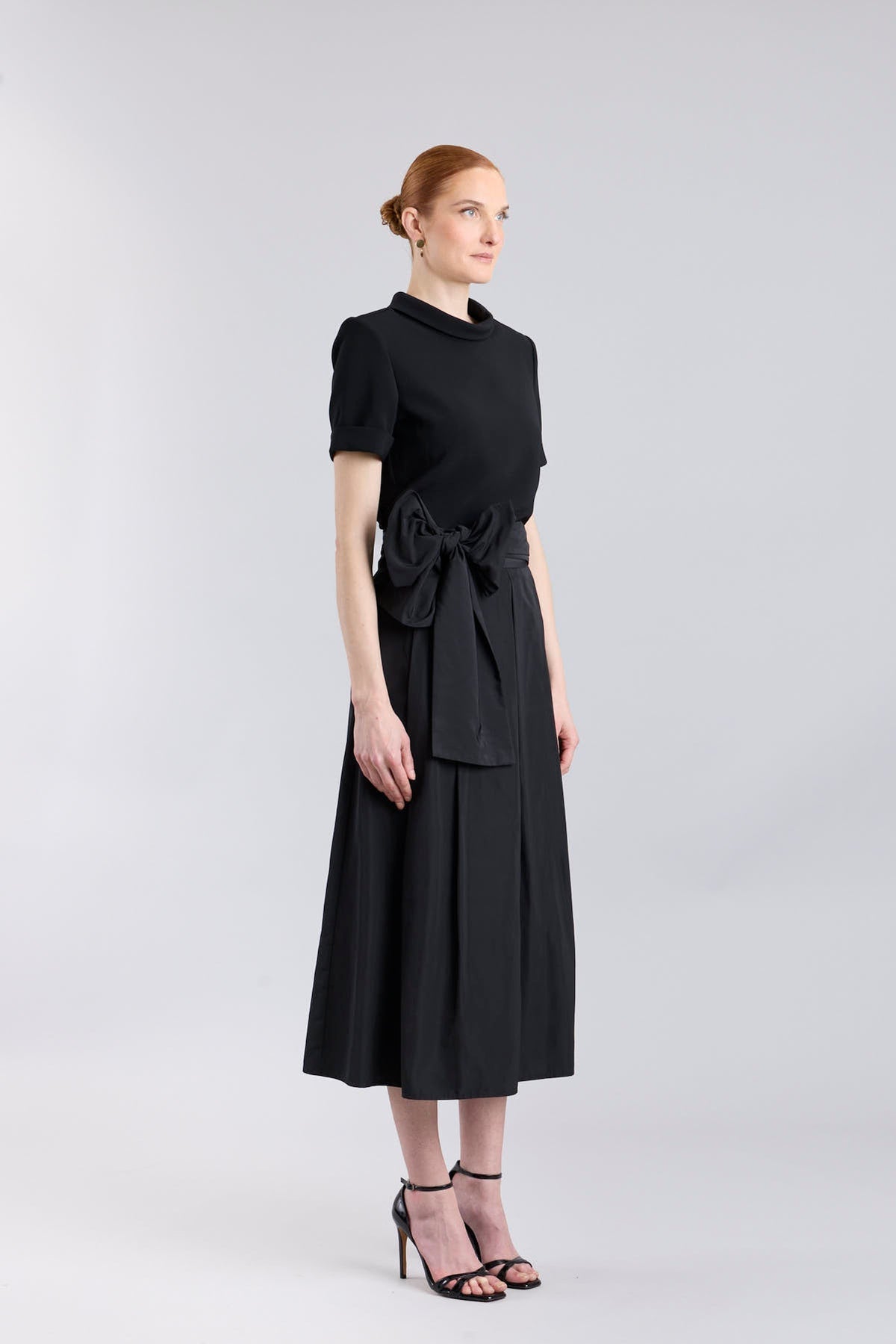 Falda midi negro estructurada con volumen teatral, corte evasé y gran lazo sastre lateral. Alta costura, exclusividad y diseño artesanal hecho en España.