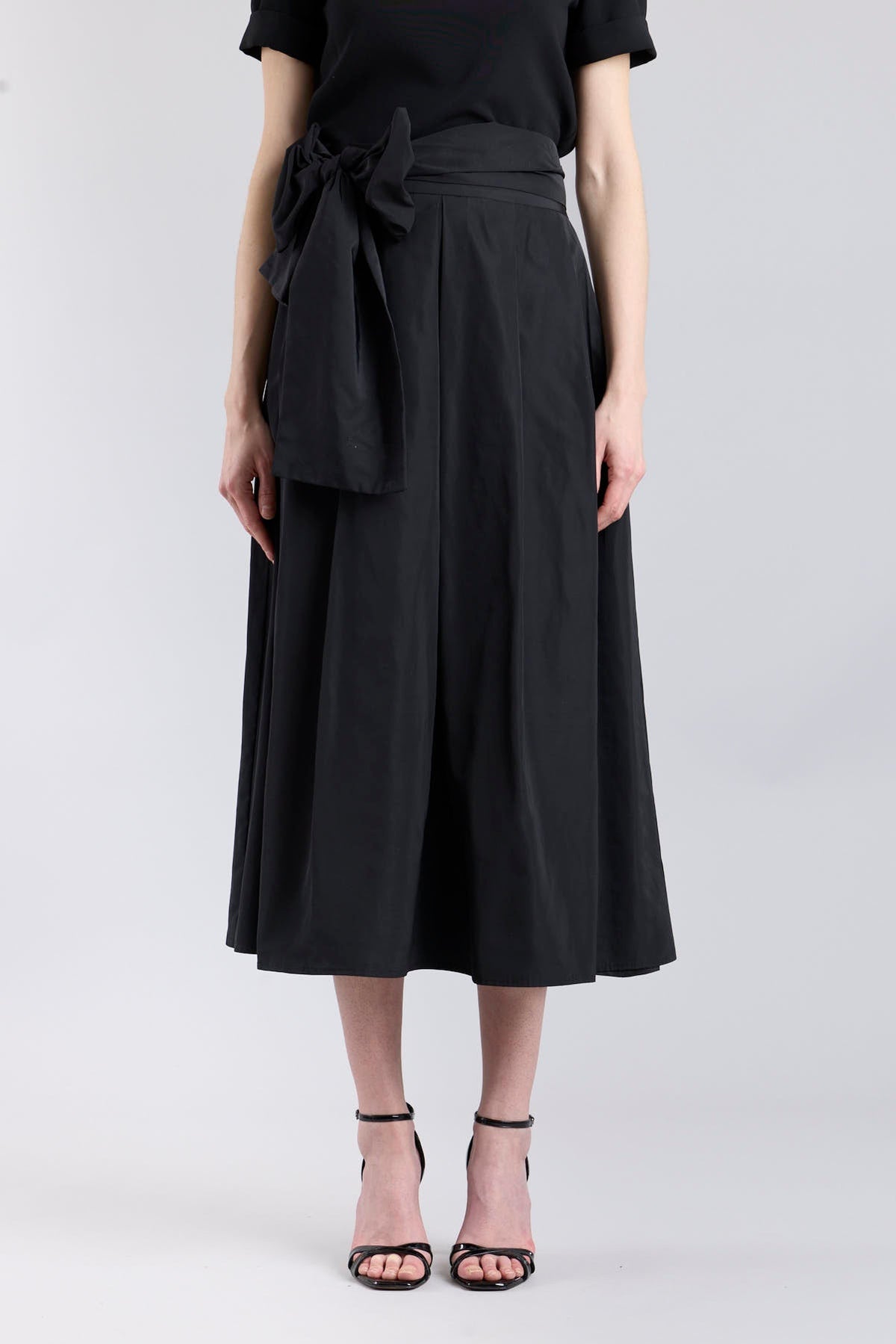 Falda midi negro estructurada con volumen teatral, corte evasé y gran lazo sastre lateral. Alta costura, exclusividad y diseño artesanal hecho en España.