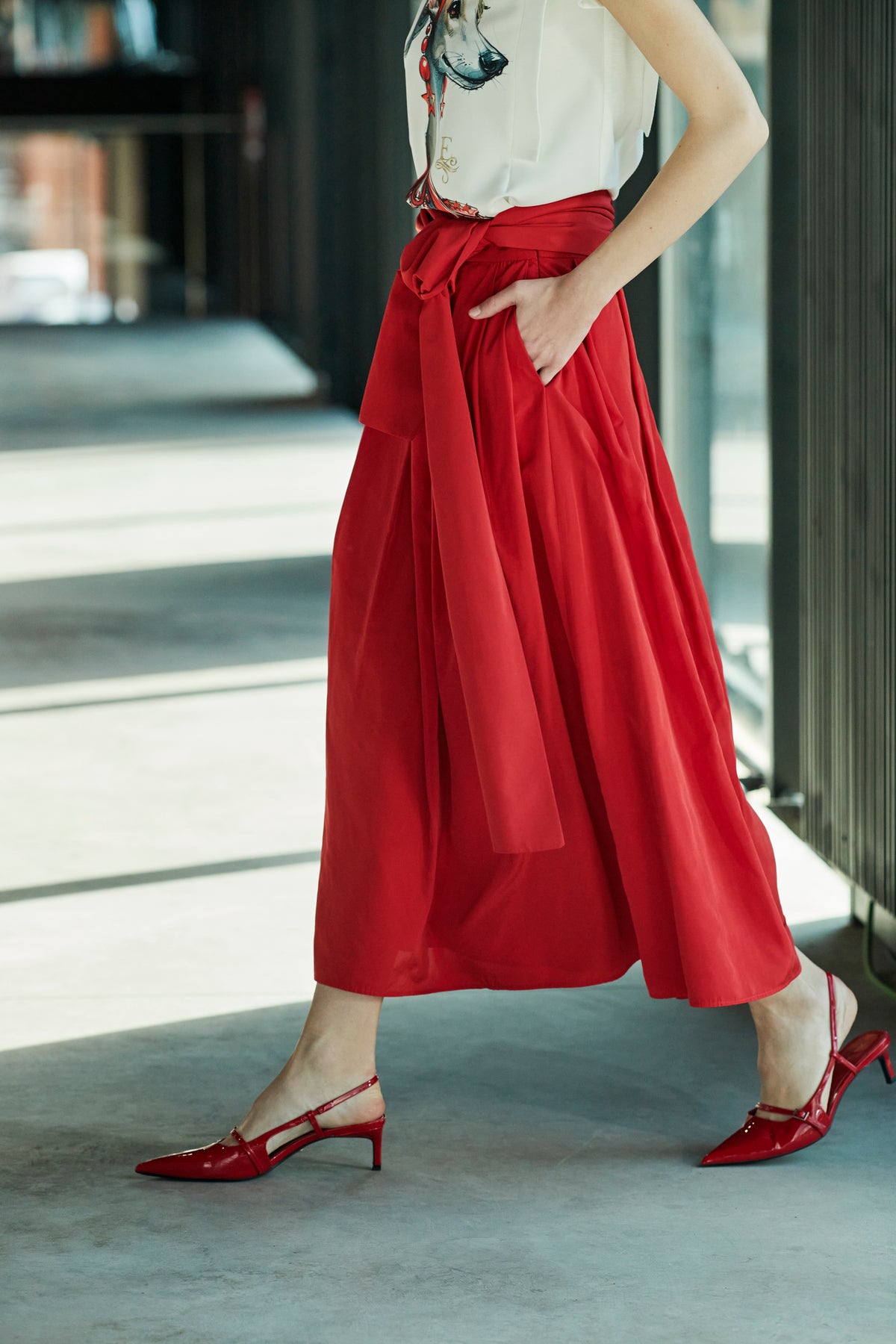Falda midi roja estructurada con volumen teatral, corte evasé y gran lazo sastre lateral. Alta costura, exclusividad y diseño artesanal hecho en España.