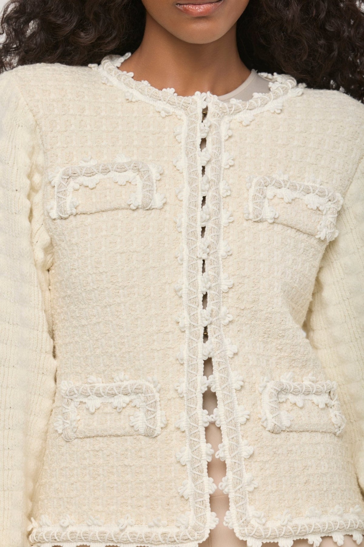 Cárdigan corto blanco de punto para mujer con estética estilo tweed, mangas abullonadas y ribetes detallados.
