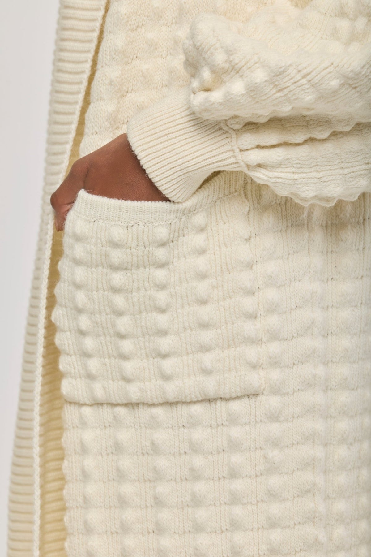 Cárdigan largo de punto blanco blanco para mujer con mangas de textura geométrica y diseño minimalista.